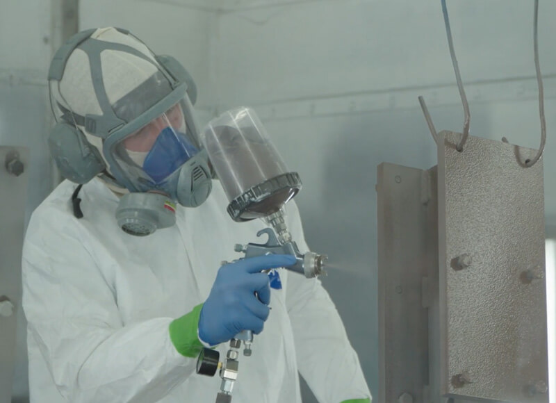 TYMETAL employee in industrial painting booth painting piece of metal