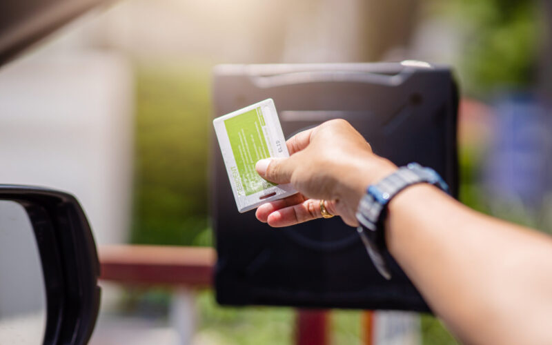 tanned arm with a multi-colored watch band using a keycard at a security gate