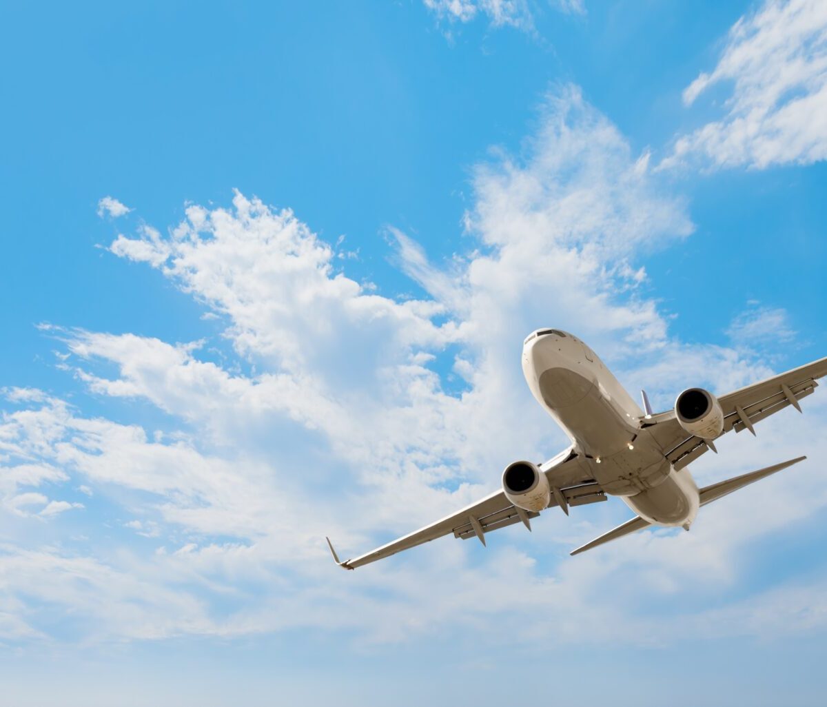 A passenger plane flies in the air with a blue sky and fluffy clouds in the background.