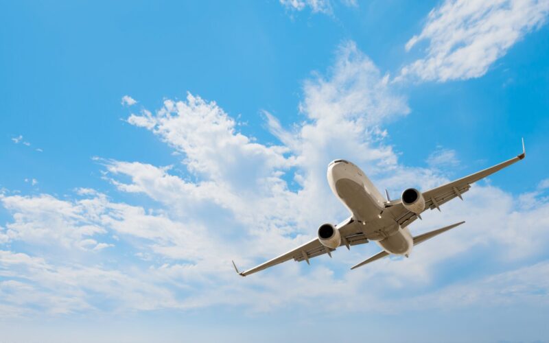 A passenger plane flies in the air with a blue sky and fluffy clouds in the background.