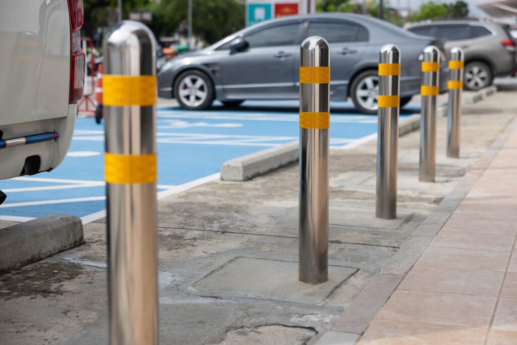 Stainless steel bollards with two yellow bands near the top separate a parking area from an unseen building 