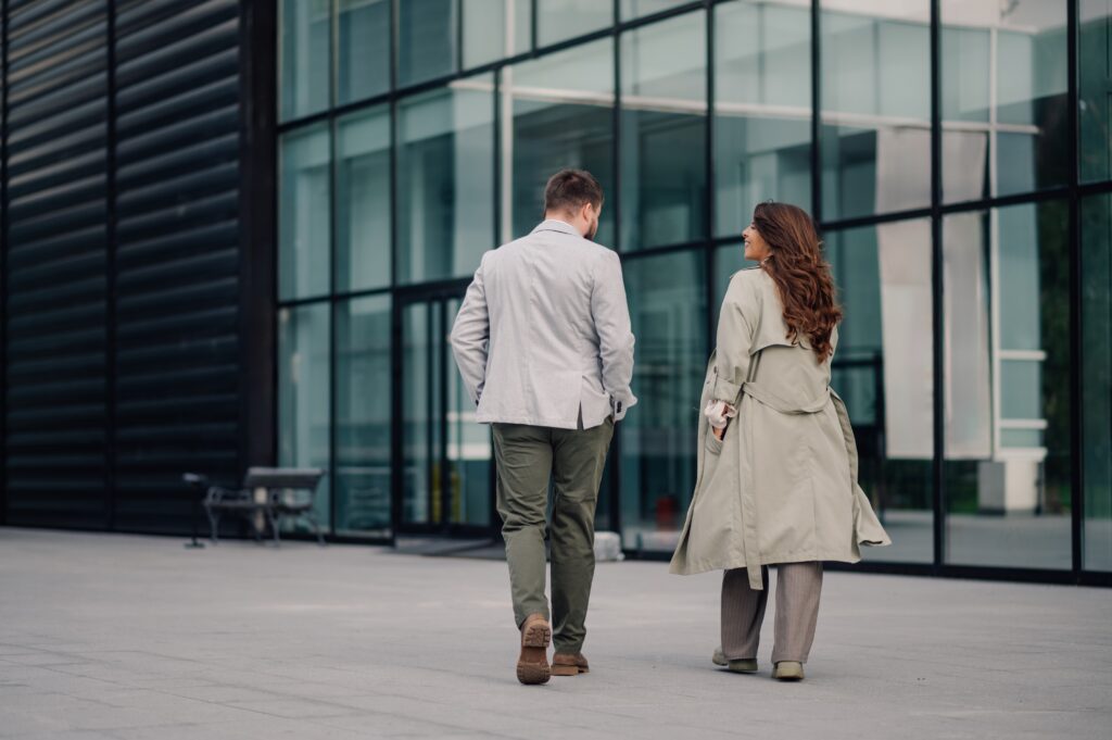 Two business colleagues walk toward the entrance of a professional building with ample glass windows and black framing