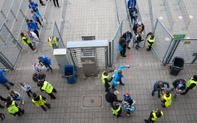 Stadium workers help to move event attendees through perimeter security gates into a stadium.