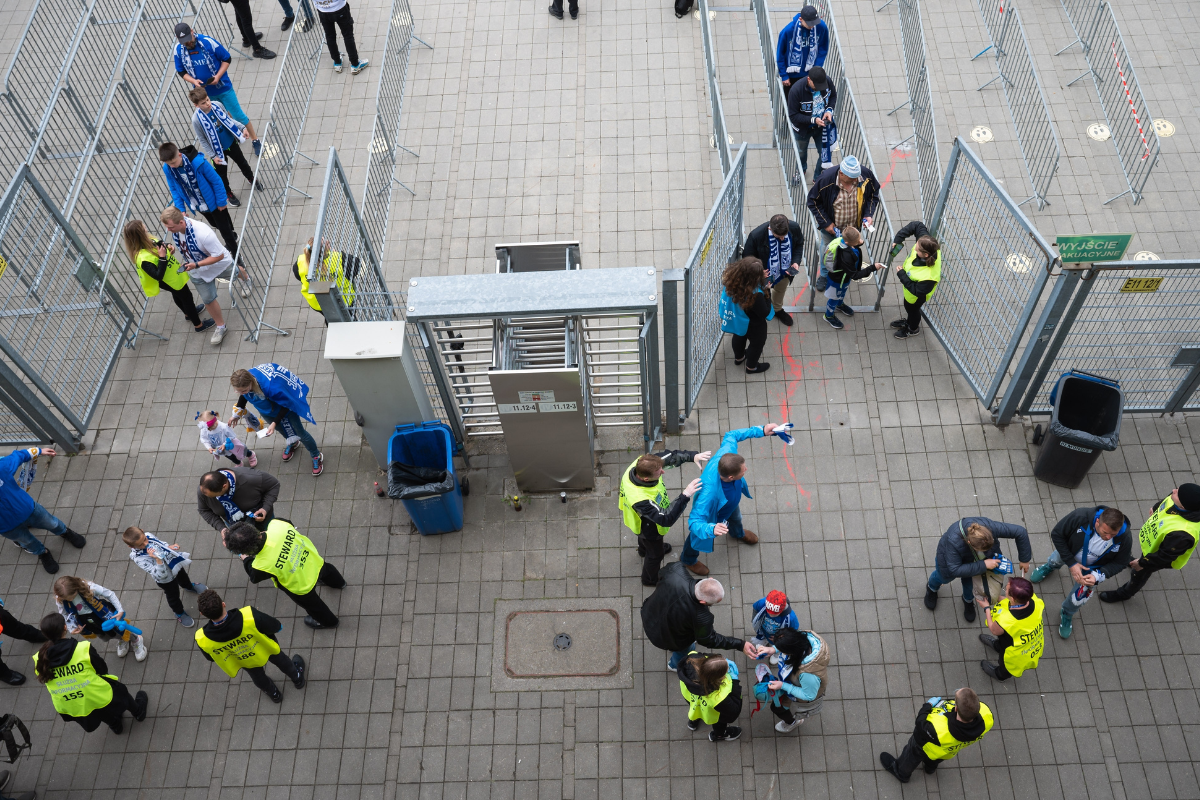 Stadium workers help to move event attendees through perimeter security gates into a stadium.